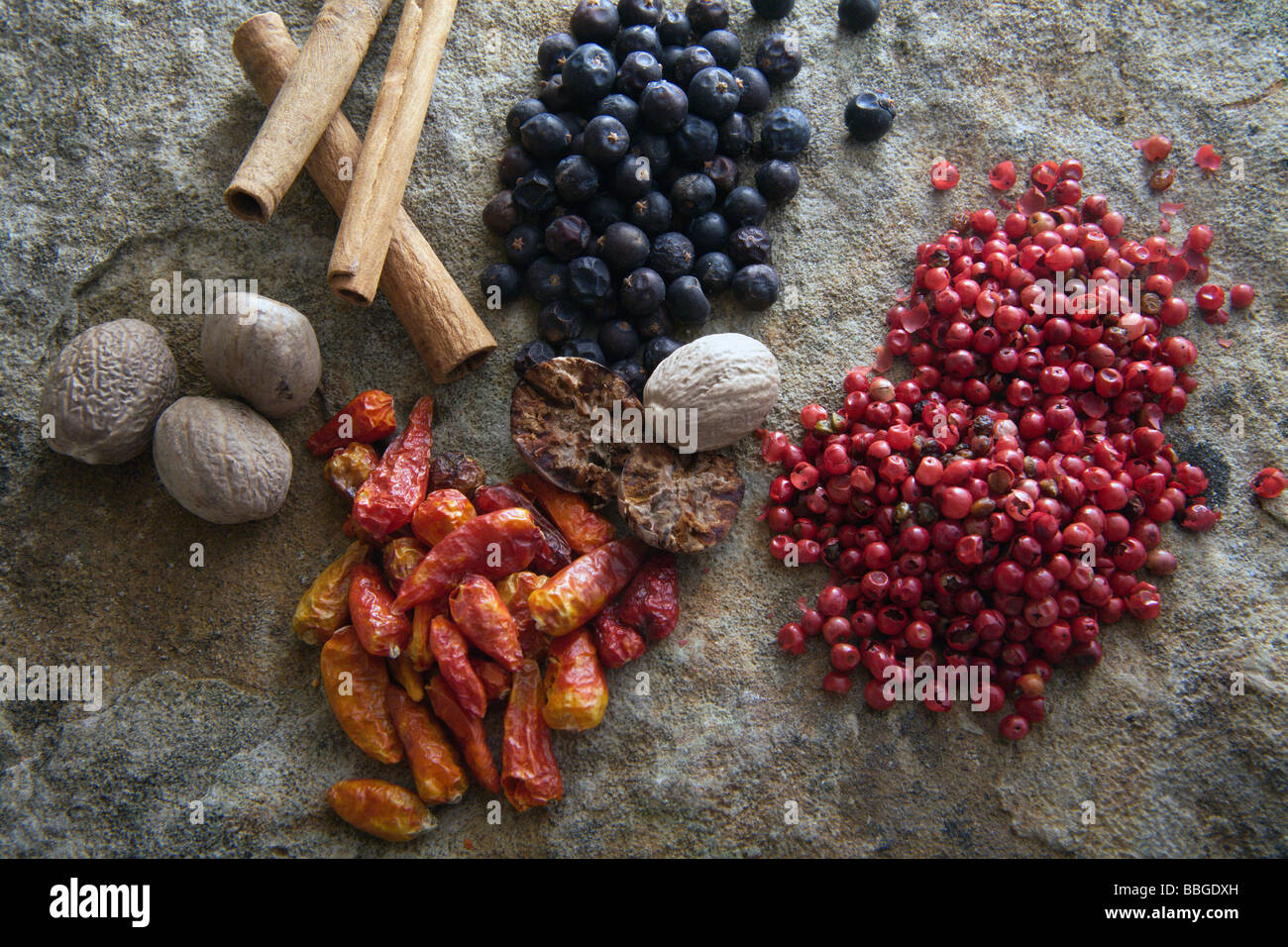 Spezie differenti su una lastra di pietra, ginepro, peperoncino, pepe rosso, noce moscata, bastoncini di cannella Foto Stock