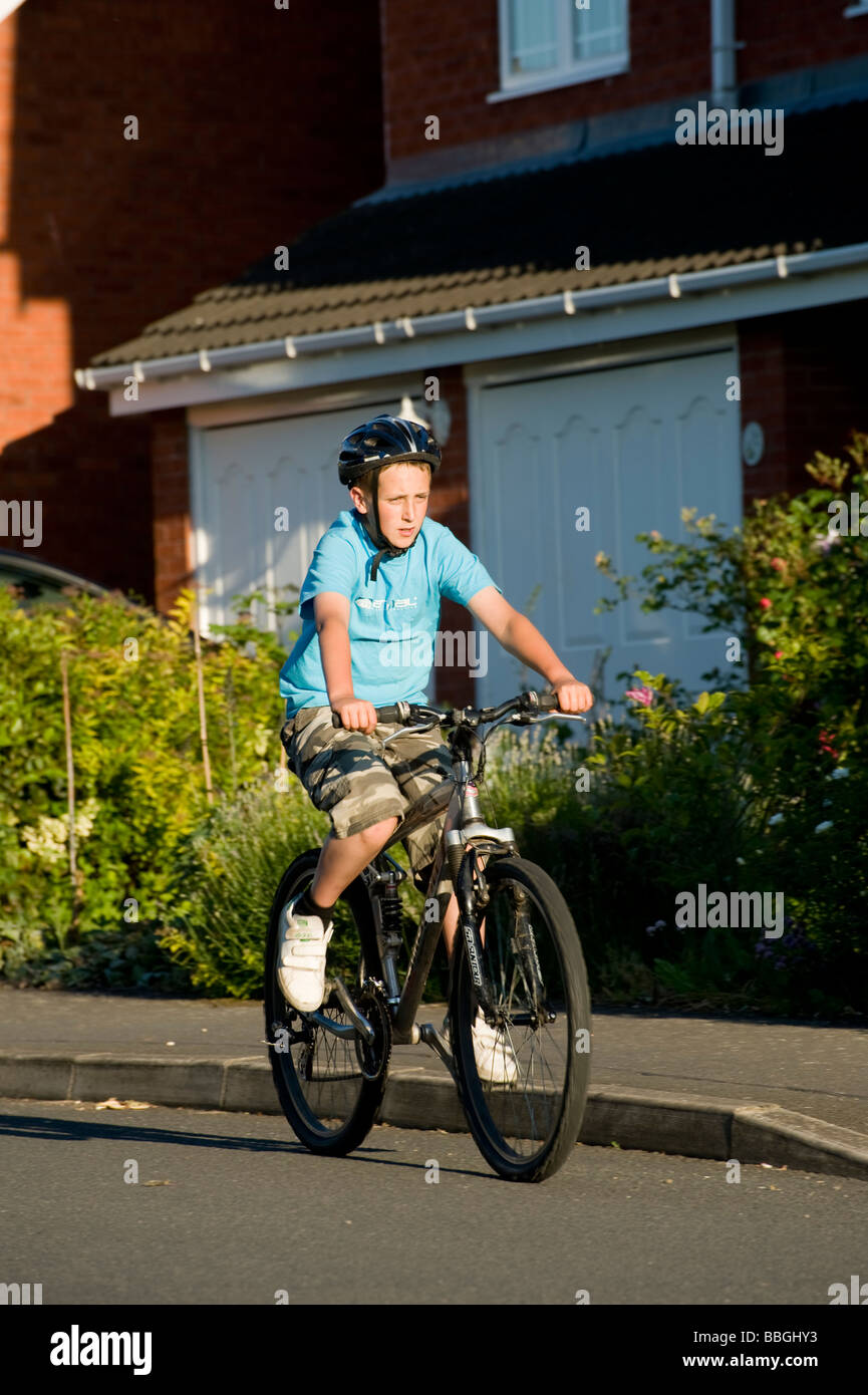 Giovane ragazzo adolescente in bicicletta lungo una strada suburbana in estate in Inghilterra Foto Stock