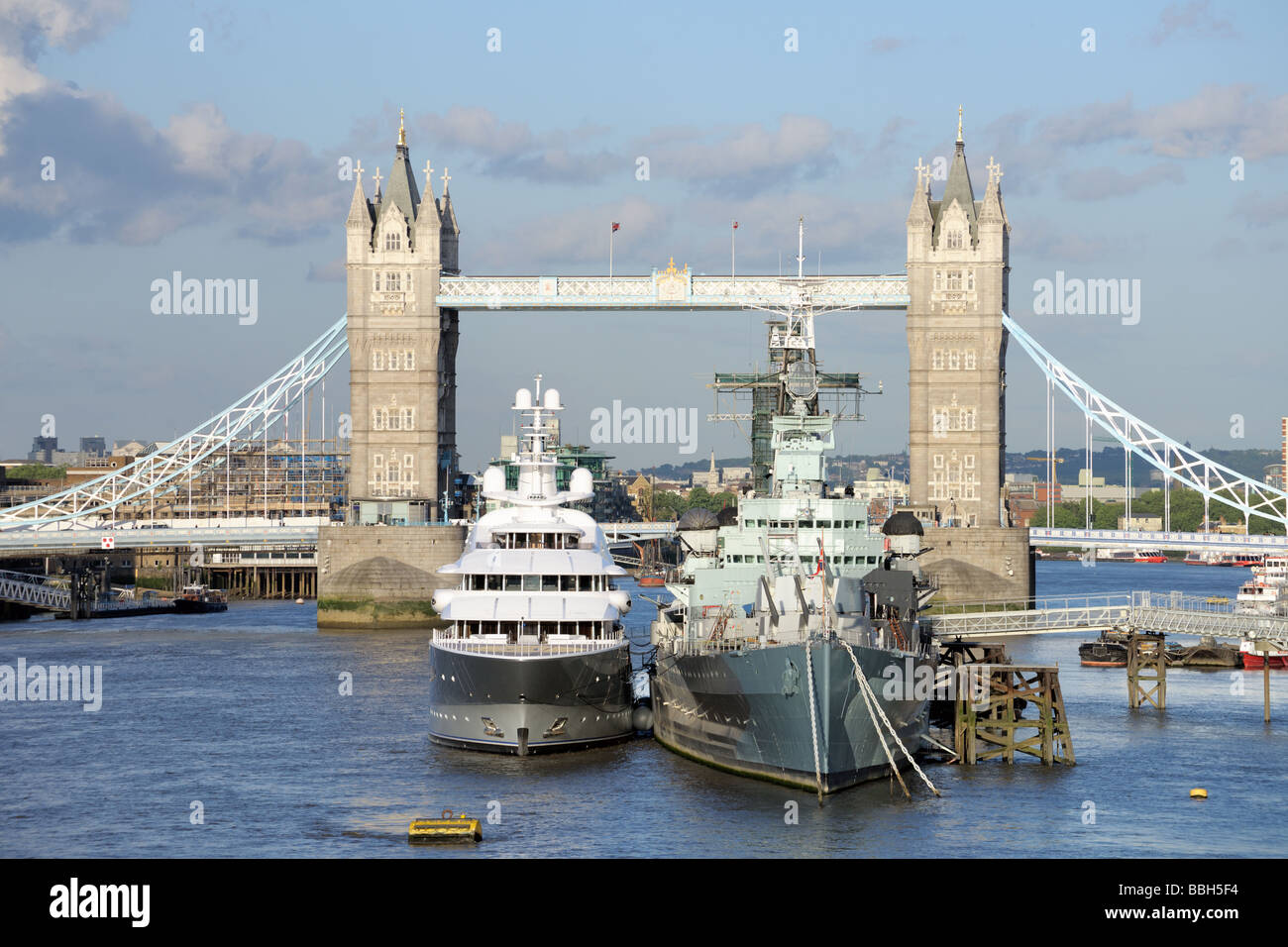 HMS Belfast e uno yacht di lusso ormeggiato sul pool di Londra, il Tamigi, con il Tower Bridge in background Foto Stock