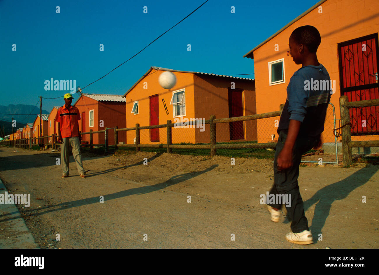 Giovani uomini giocare a calcio sulla strada fuori Piazza Fatyela Lwandle South Western Cape Sud Africa Foto Stock