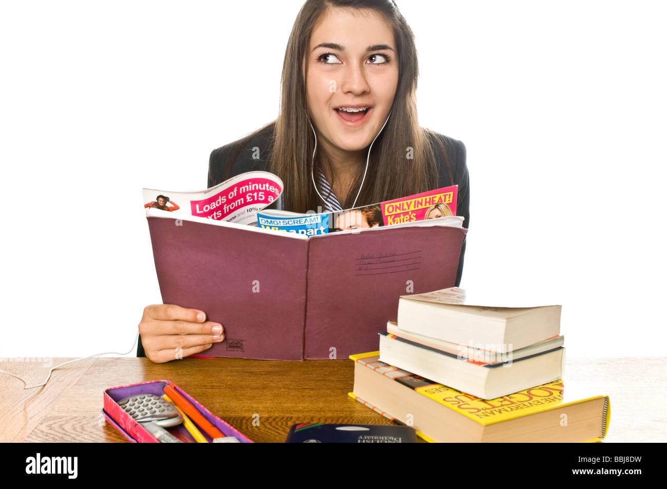 Umoristico ritratto orizzontale di una scuola teenage girl catturati fuori leggendo una rivista e ascoltare il suo ipod dietro il suo libro Foto Stock