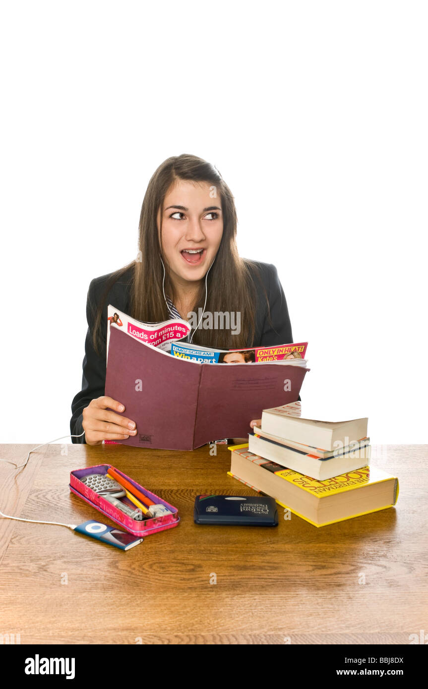 Umoristico ritratto verticale di un attraente ragazza adolescente alla sua scrivania segretamente leggendo una rivista dietro il suo libro scolastico Foto Stock