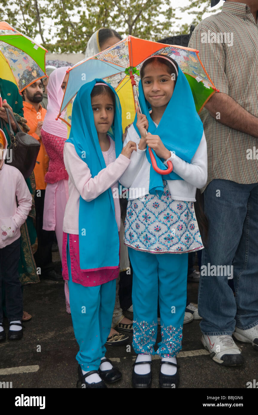 Due giovani ragazze Sikh riparo sotto un ombrello per guardare il Vaisakhi processione in Manor Park, Londra. Foto Stock