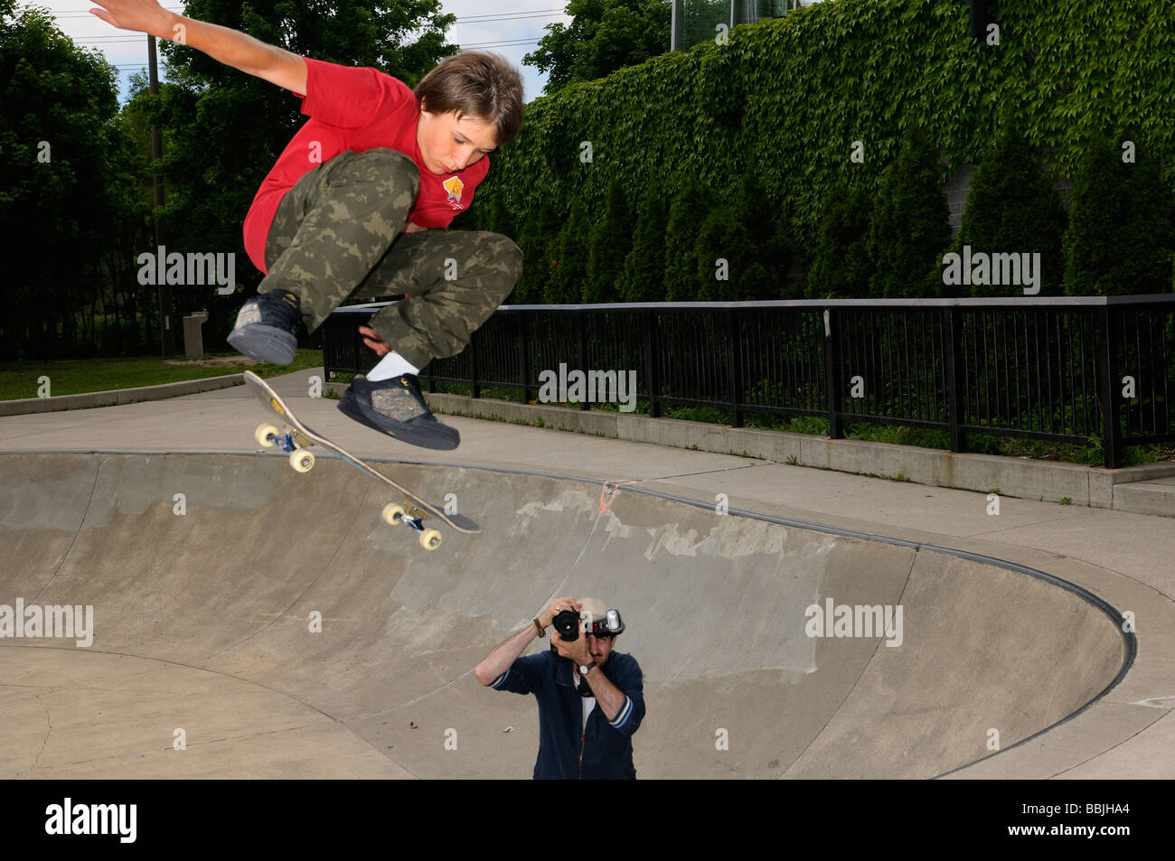 Ragazzo giovane airborne su uno skateboard al di sopra di un recipiente di calcestruzzo in un esterno di Toronto park con il fotografo Foto Stock