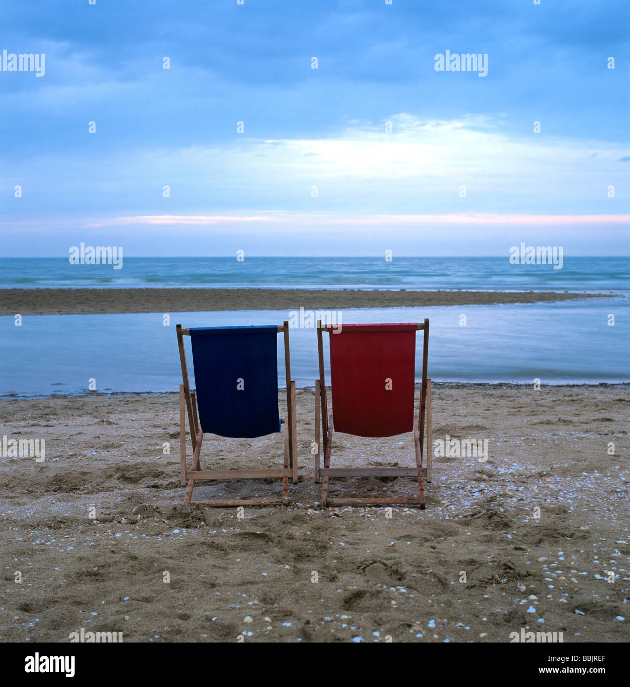 Due sdraio in legno sulla spiaggia di fronte al mare al tramonto / Crepuscolo Foto Stock