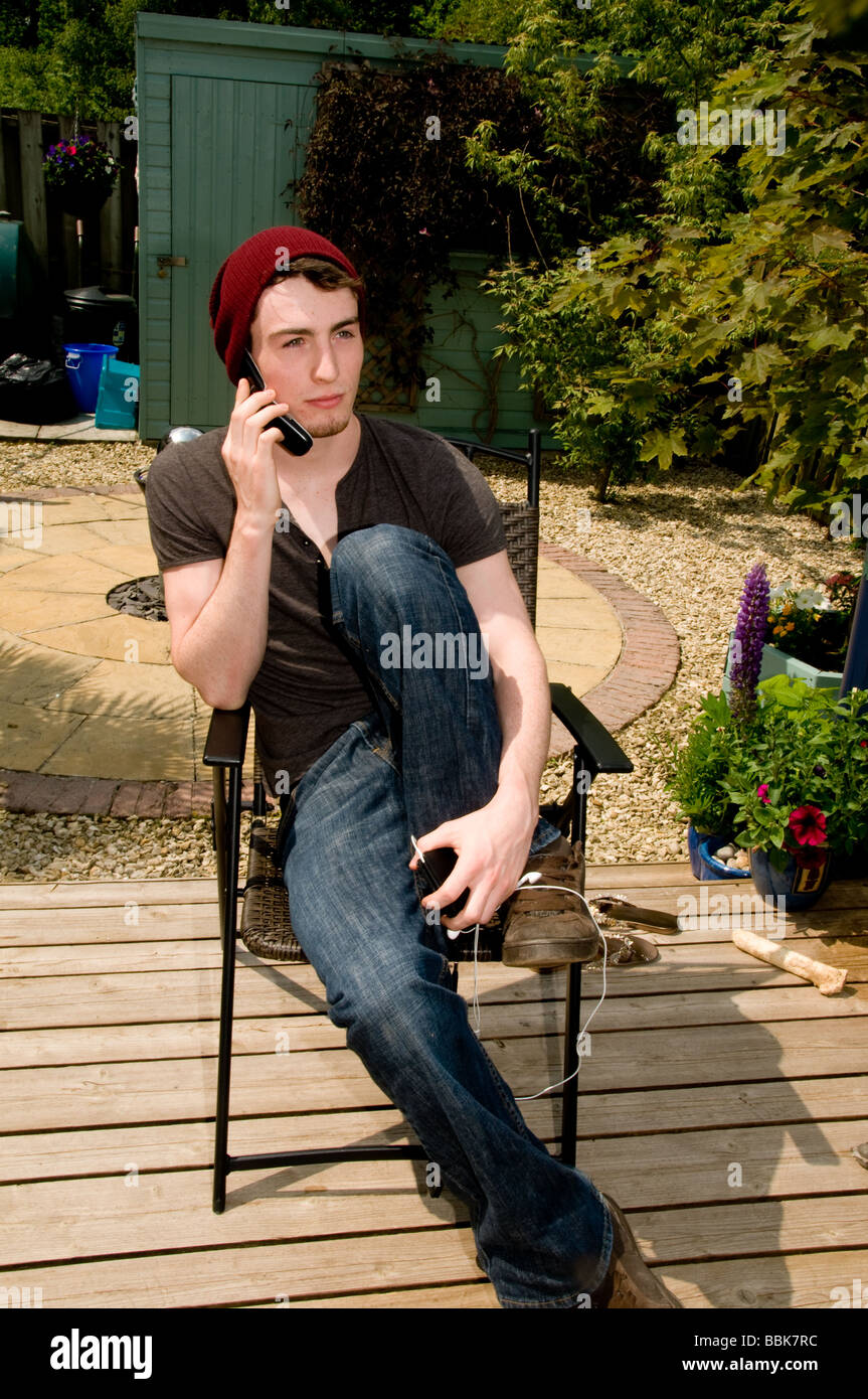Giovane uomo seduto in una sedia a sdraio con Red Hat a parlare al telefono con i pod Foto Stock