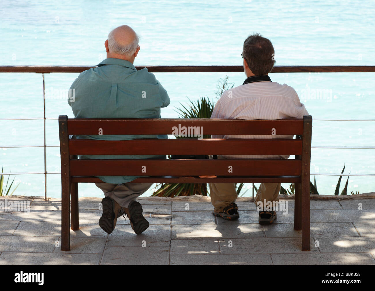 Due uomini seduti su una panchina pubblica in Sant Elm affacciato sul mare in Maiorca Foto Stock