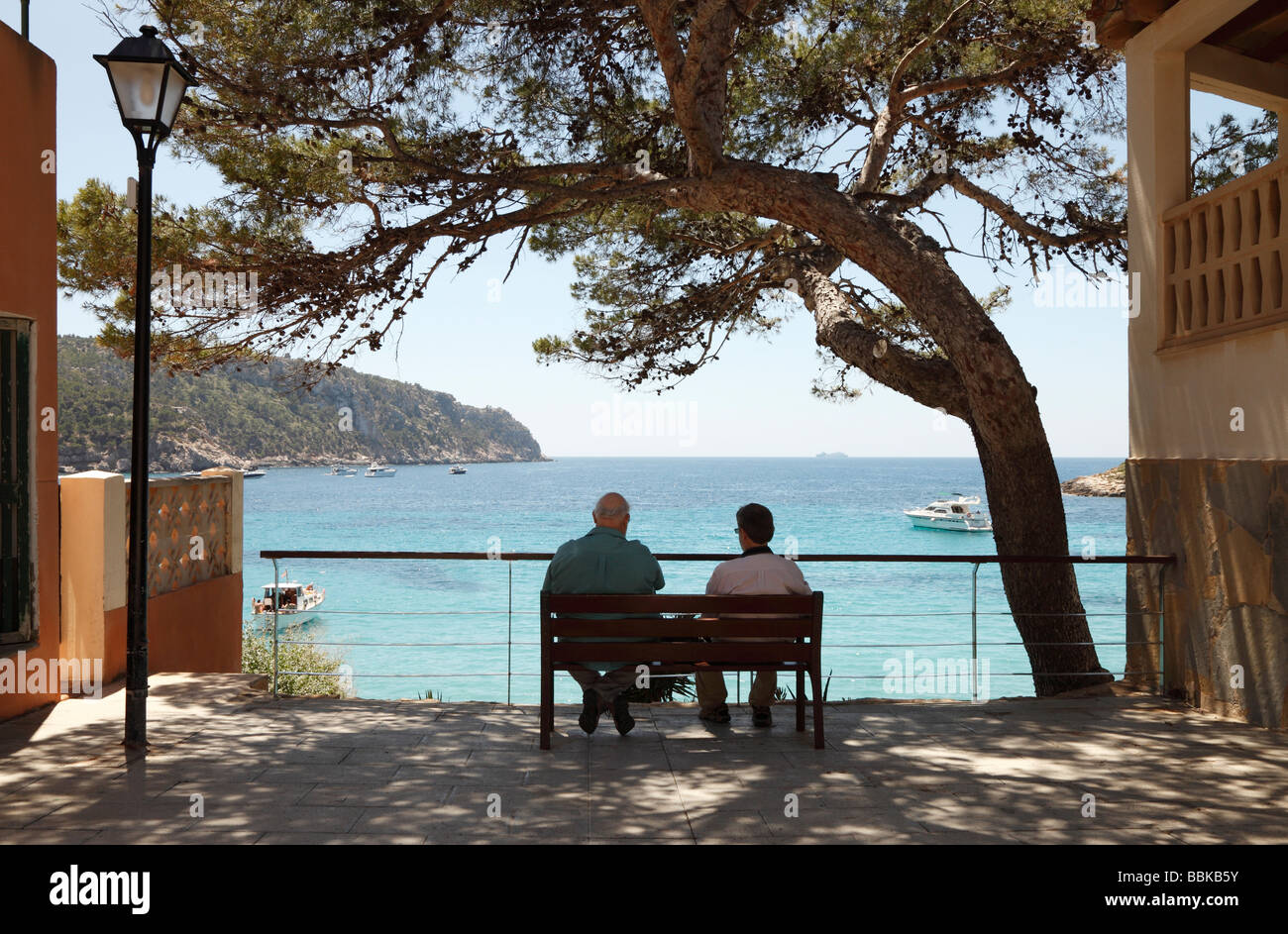 Due uomini seduti su una panchina pubblica in Sant Elm affacciato sul mare in Maiorca Foto Stock