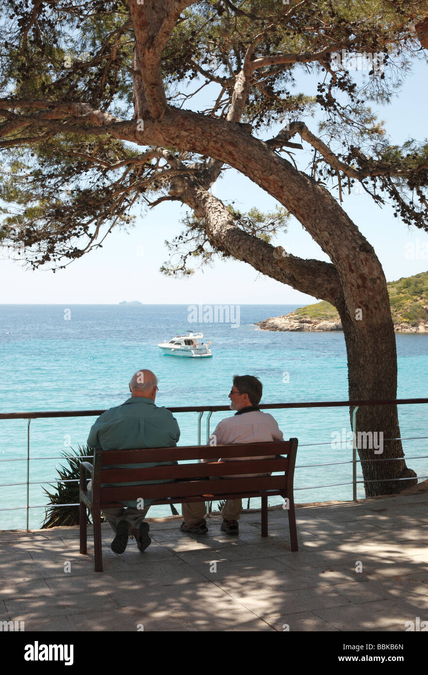 Due uomini seduti su una panchina pubblica in Sant Elm in western Mallorca affacciato sul mare Foto Stock