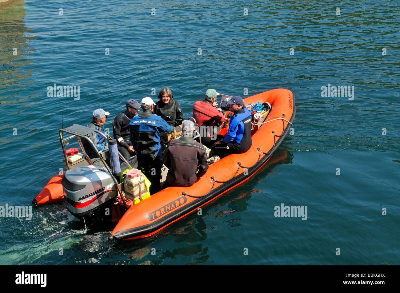I subacquei sulla costola arancione motoscafo fuoribordo riempito con persone accelerando in acqua Foto Stock