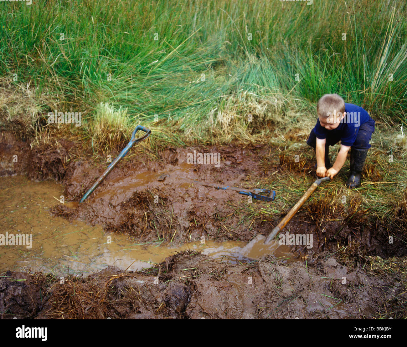 Lo scavo di un laghetto della fauna selvatica utilizzando i giovani aiutanti Foto Stock