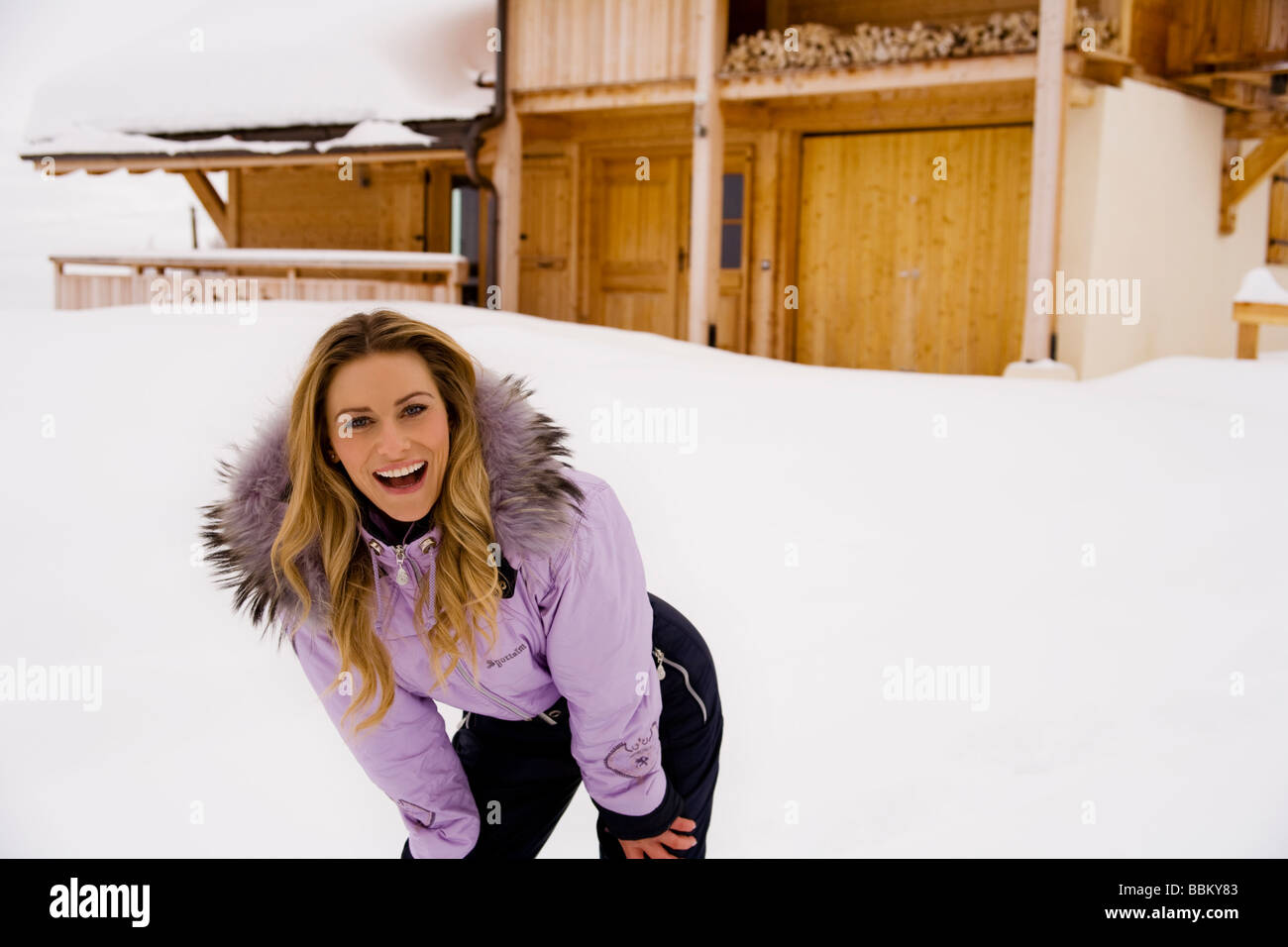 Una giovane donna bionda mantiene caldo nella neve di un ski resort chalet complesso. Foto Stock