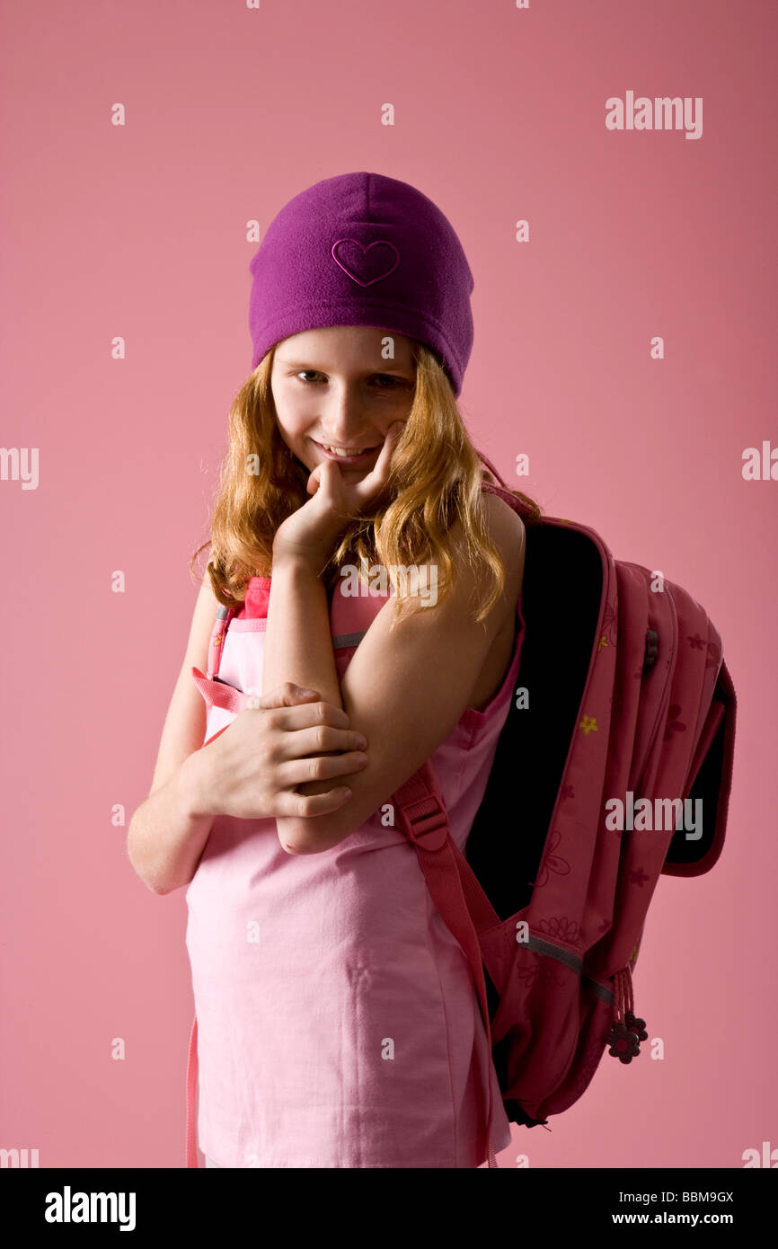 I Capelli rossi ragazza indossando un viola cofano e zainetto davanti a uno sfondo di colore rosa Foto Stock