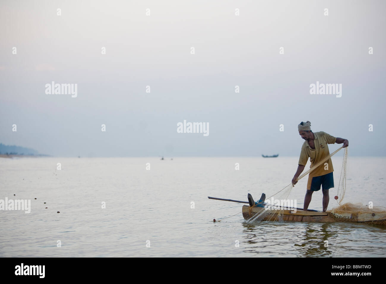 Indiano pescatore di sussistenza in trazione le sue reti da fatti a mano la barca di legno vicino alla riva. Foto Stock