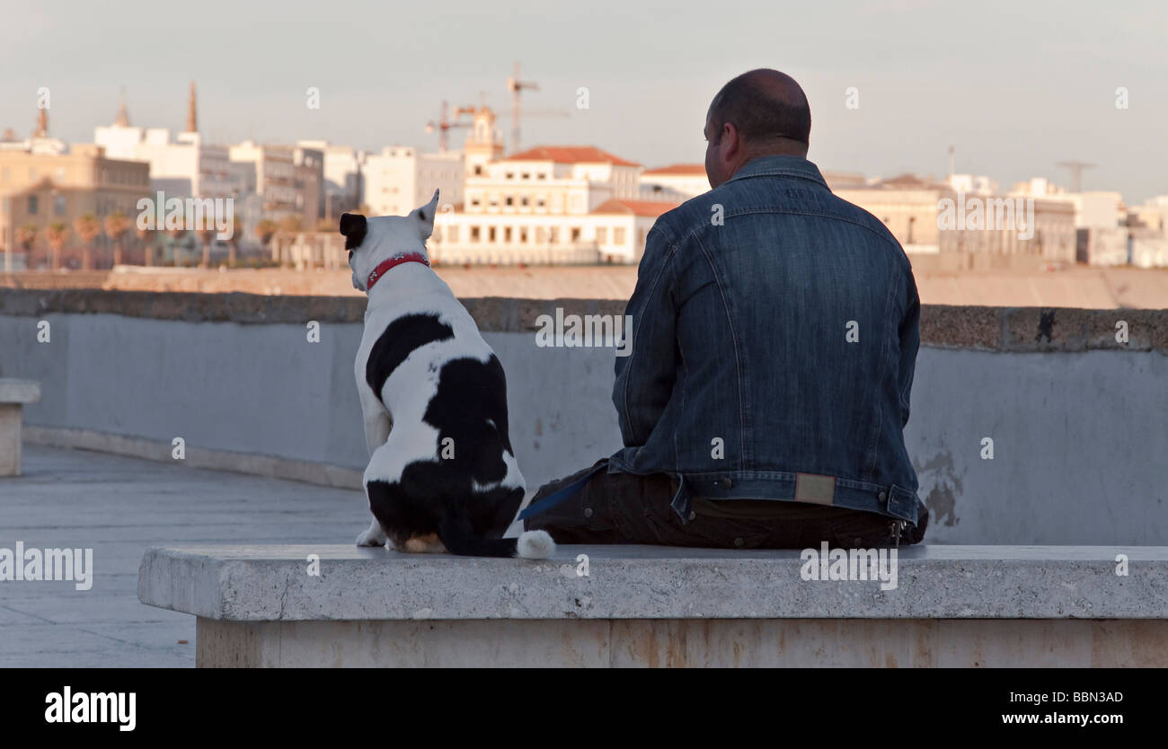 Uomo e cane seduti su un banco di marmo presso il lungomare a Cadice, Andalusia, Spagna, Europa Foto Stock