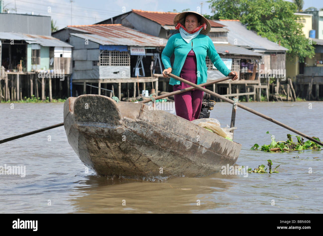 Donna con cappello tradizionale a forma di cono hat fatte di foglie di palma, permanente e la barca a remi di una barca di legno sul Mekong, carico di frutta Foto Stock