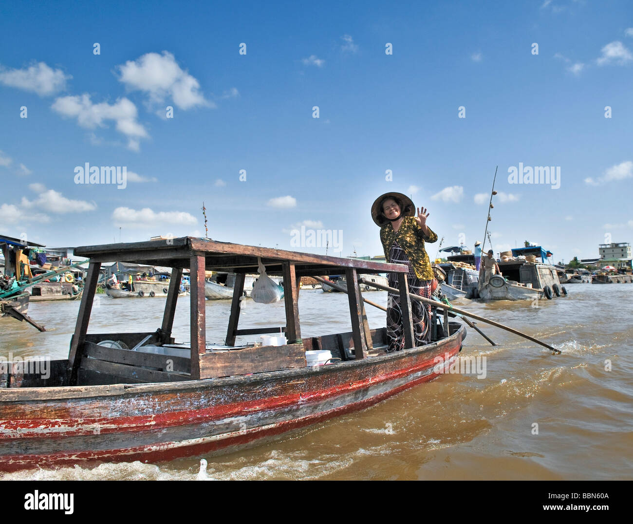 Donna con cappello tradizionale a forma di cono hat fatte di foglie di palma, permanente e la barca a remi di una barca di legno sul Mekong, Delta del Mekong, Foto Stock