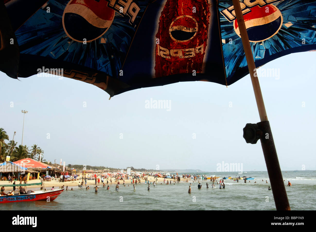 Un ombrello e un affollato Baga Beach nel nord di Goa in India Foto Stock