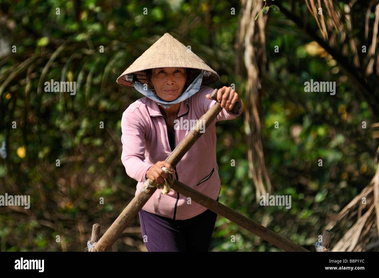 Donna con un tradizionale cappello a forma di cono hat fatte di foglie di palma, remare una barca di legno pieno di frutta sul Mekong, Can Tho, M Foto Stock