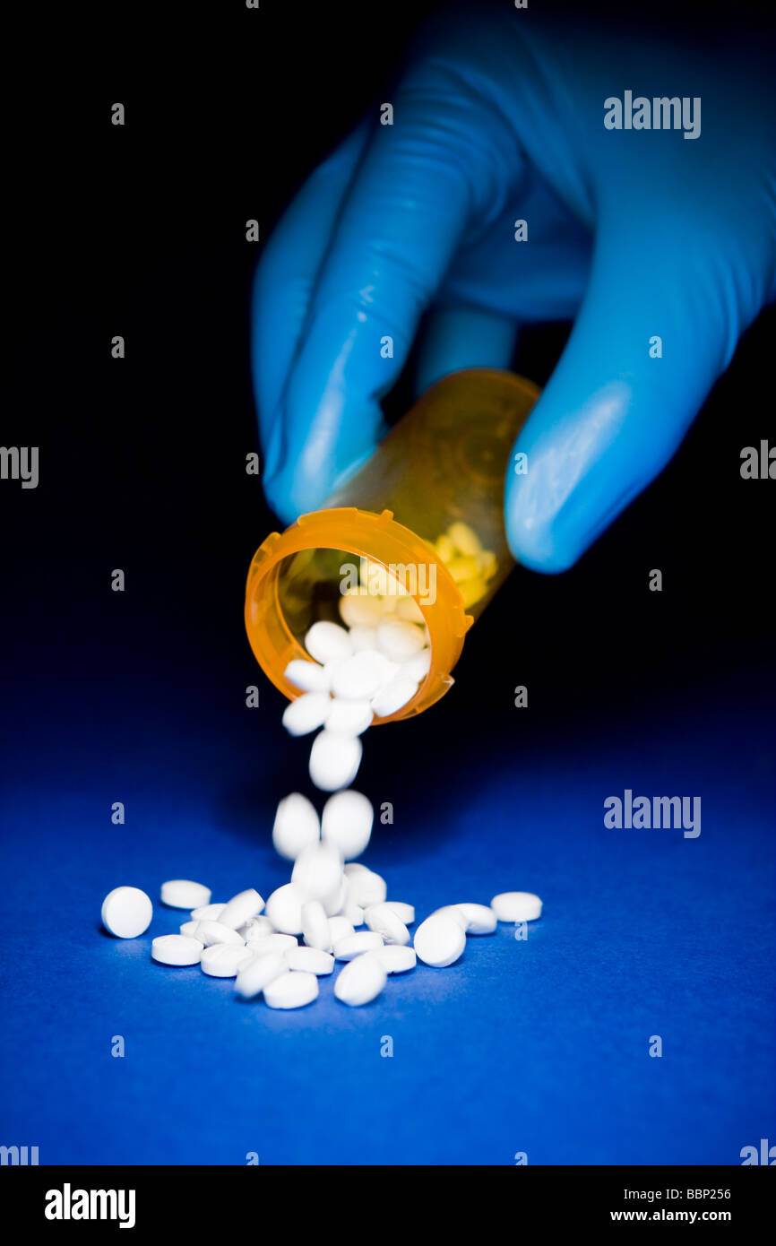 Close-up di una mano in una blu guanto chirurgico lo svuotamento di un arancione bottiglia di Prescrizione di pillole di bianco Foto Stock