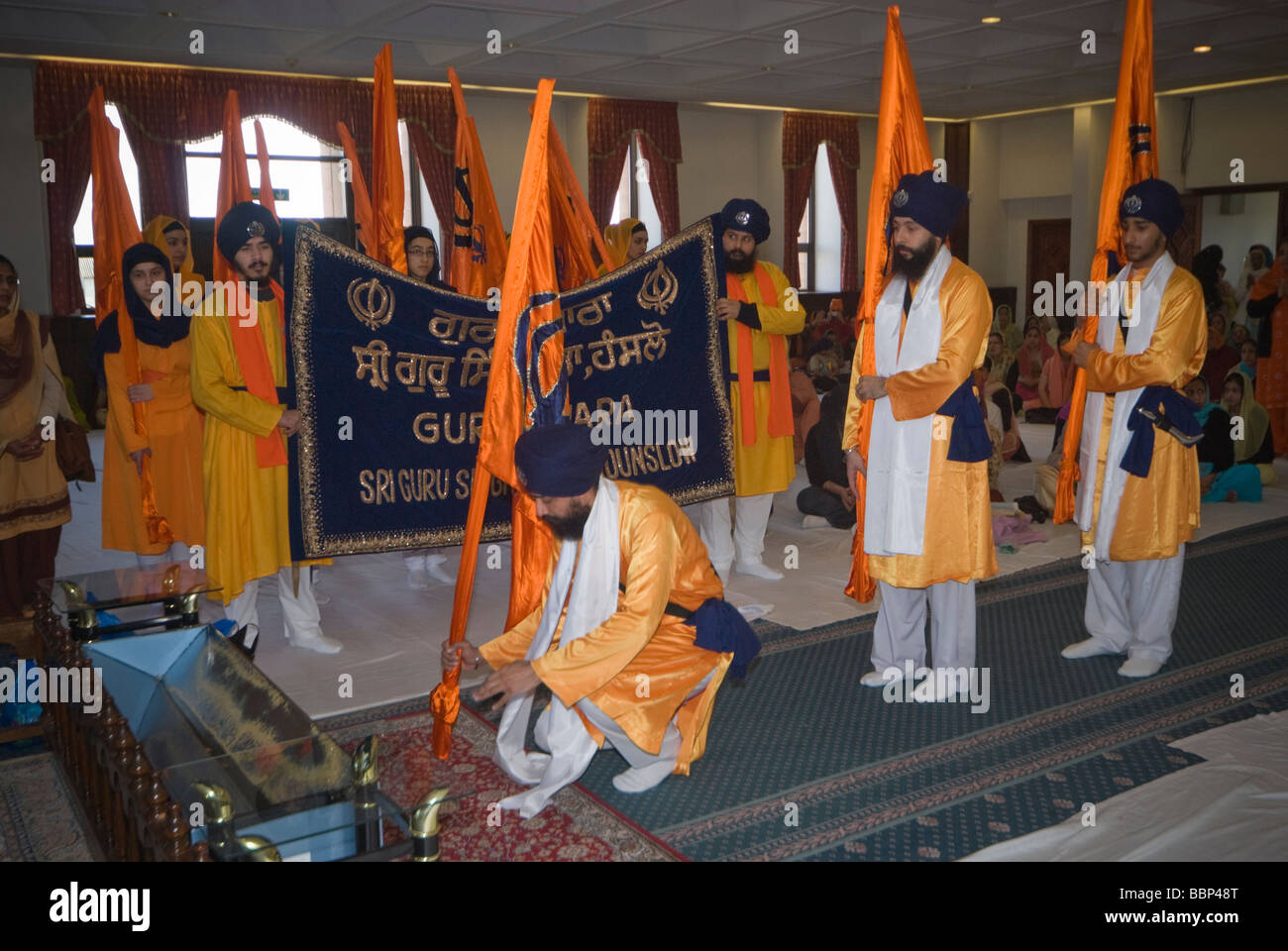 I sikh in sala culto a Hounslow Gurdwara per celebrazioni Vaisakhi . Gli uomini che trasportano le bandiere Sikh prua al Guru Granth Sahib Foto Stock