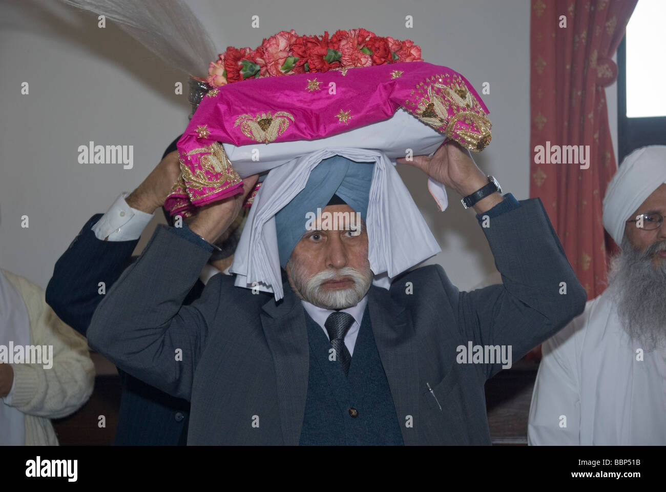 I sikh in Hounslow prendere parte in Vaisakhi celebrazioni e una processione. Un uomo porta il Guru Granth Sahib sulla sua testa. Foto Stock