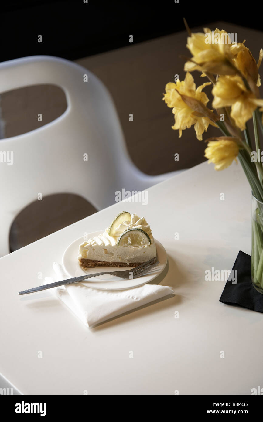 Gateau sulla piastra con la forcella sul tavolo nel ristorante con sedia bianca e un tavolo e narcisi Foto Stock