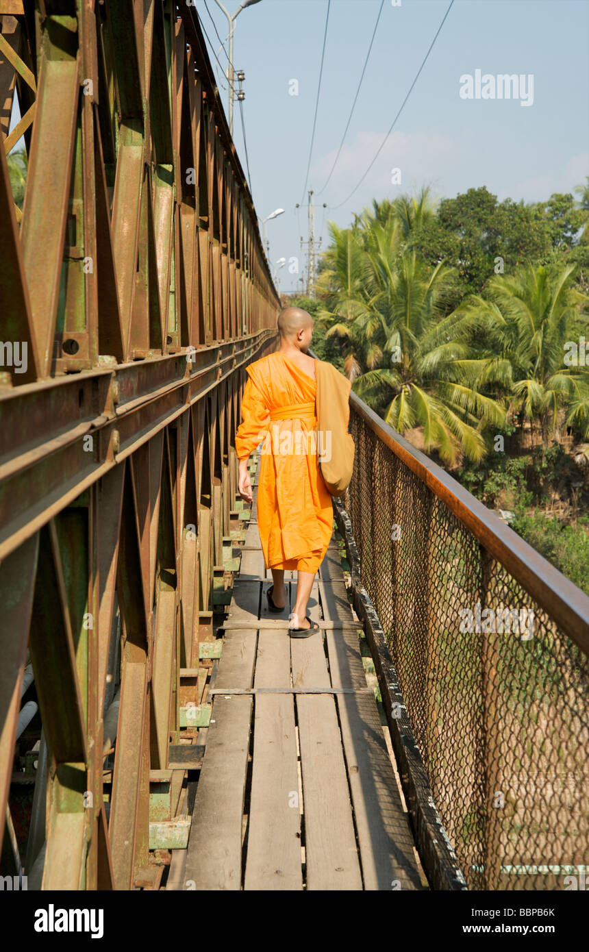 Un monaco buddista passeggiate attraverso il Sisavangvong ponte che si estende attraverso il fiume Nam Khan a Luang Prabang, Laos Foto Stock