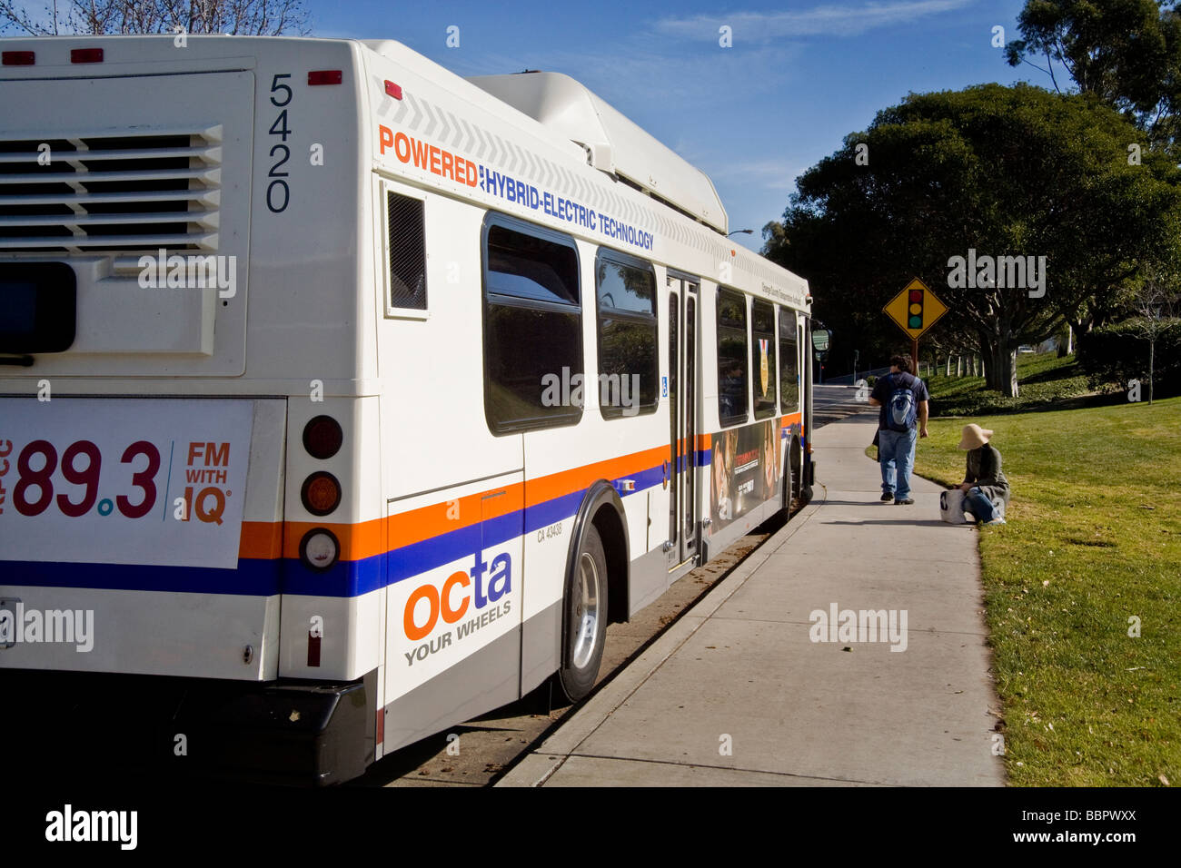 Utilizzando un basso inquinamento gas naturale ibrido elettrico la potenza di un autobus urbano attende i passeggeri a Irvine California USA Foto Stock
