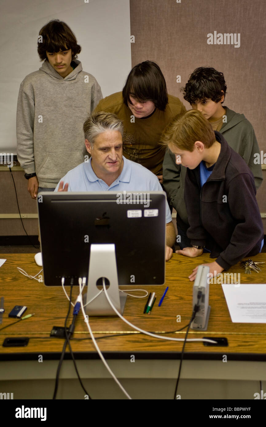 Gli studenti delle scuole medie guarda il monitor come i loro computer insegnante di classe mostra loro nuovo software Foto Stock