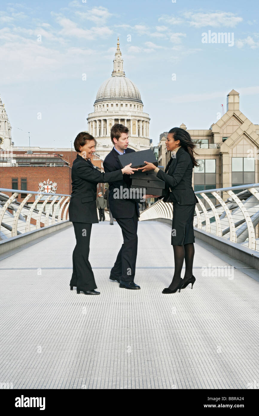 Tre persone di affari (due femmina, un maschio) sul millennio lottando per contenere una pila di scatole di file, Foto Stock
