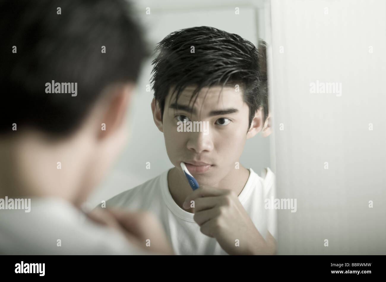 Giovane uomo spazzolatura dei denti, guardando il riflesso dello specchio Foto Stock