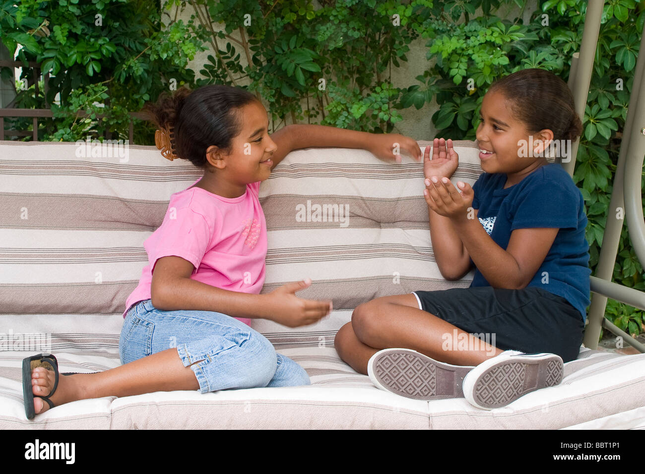 Giovane gente due americano africano sorelle 6-7 anni, 8-9 anni seduto sul divano altalena per bambini all'aperto in chat chat signor © Myrleen Pearson Foto Stock