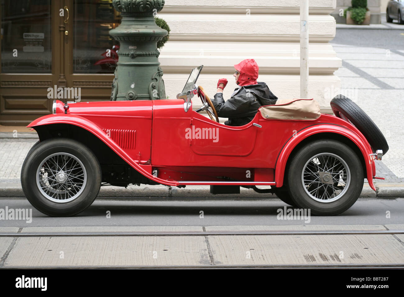 Aero 1000 rosso vintage del 1933 o del 1934 parcheggiato in una strada della città con un autista in berretto rosso e una giacca nera seduto al volante Foto Stock