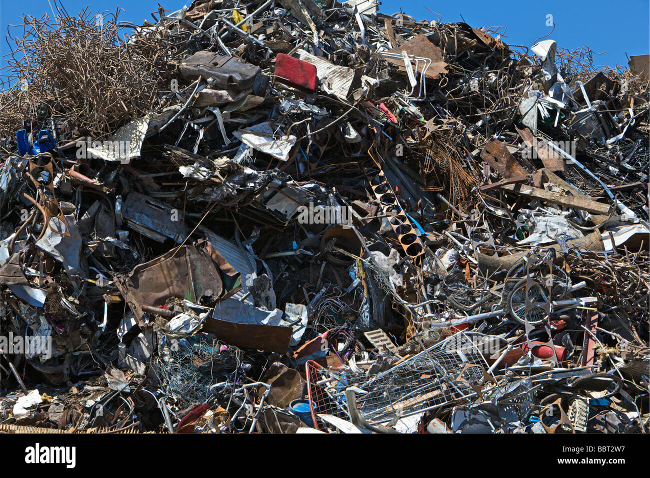Un mucchio di rottami misti metalli in attesa di elaborazione a un centro di riciclaggio set contro il profondo blu del cielo Foto Stock