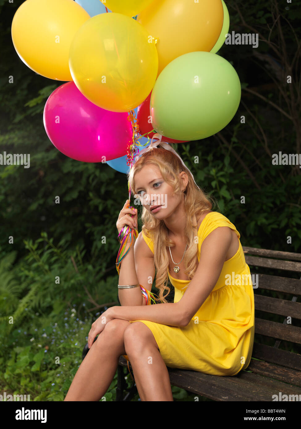 Triste giovane donna seduta su una panchina con un mucchio di palloncini colorati Foto Stock