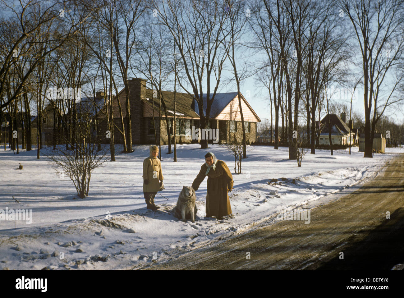 Madre e figlia con un Husky nella neve davanti di smart nuovo alloggiamento, Canada 1956 Foto Stock