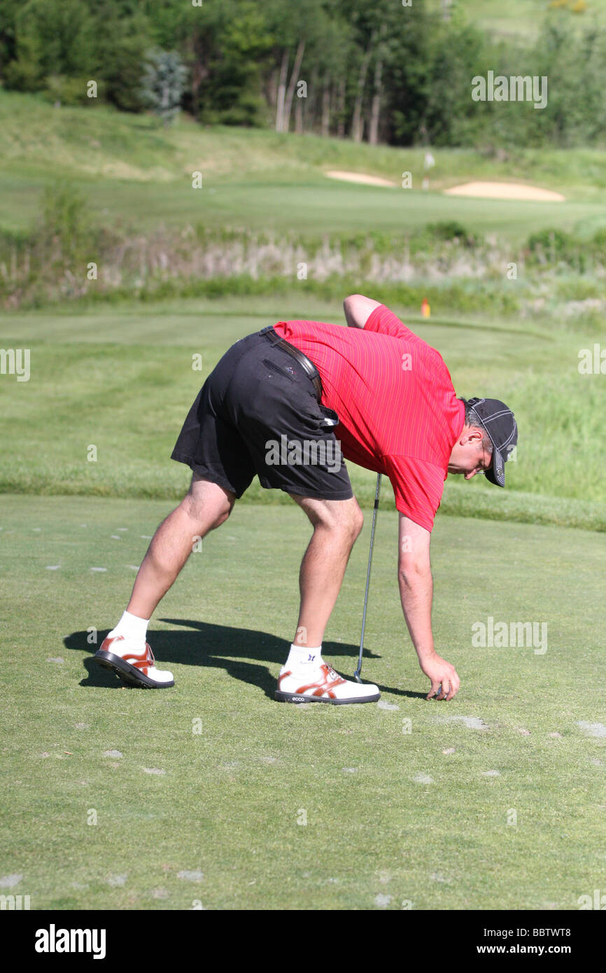 Un maschio adulto giocatore di golf tees fino la sua pallina da golf tra il raccordo a t i marcatori sul raccordo a T della scatola di un par 3 prima di colpire il suo tee-shot. Foto Stock