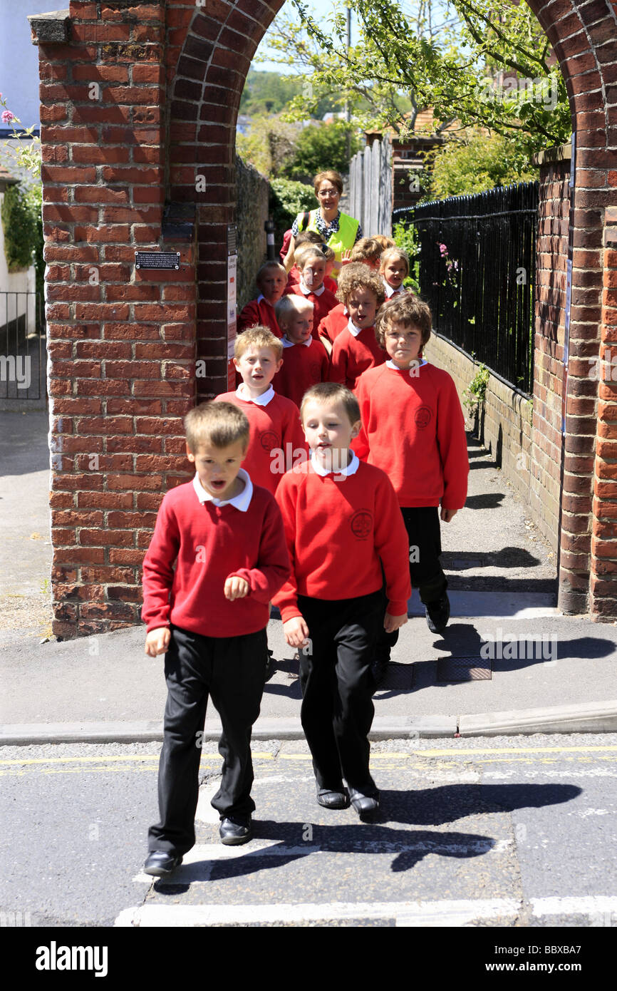Inglese Scuola Junior bambini attraversare una strada principale con la supervisione di insegnanti presso la parte anteriore e posteriore del gruppo Foto Stock