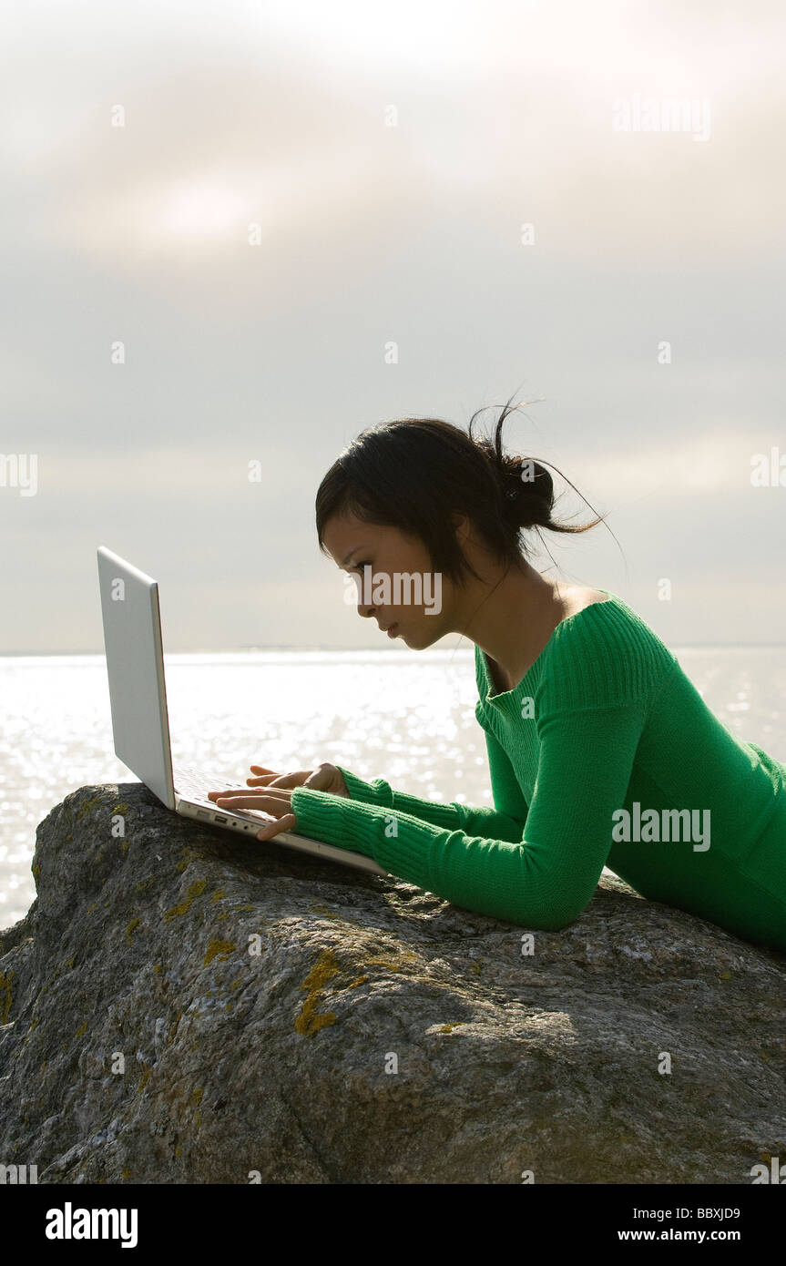 Una giovane donna su una roccia con un computer portatile in Svezia. Foto Stock