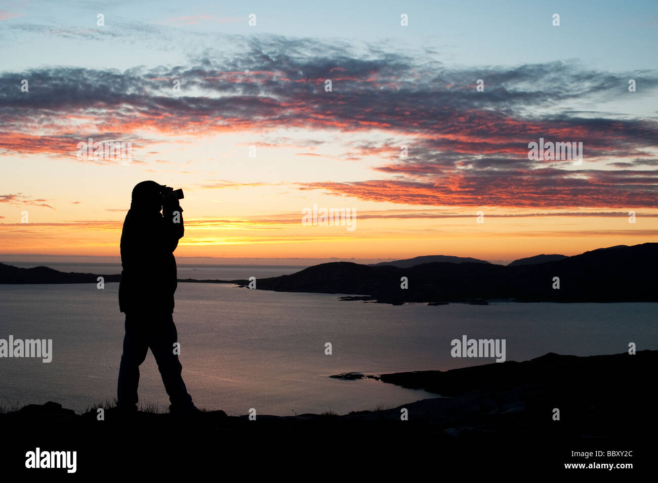 Silhouette di un fotografo al tramonto guardando sopra Taransay Isola, Isle of Harris, Ebridi Esterne, Scozia Foto Stock