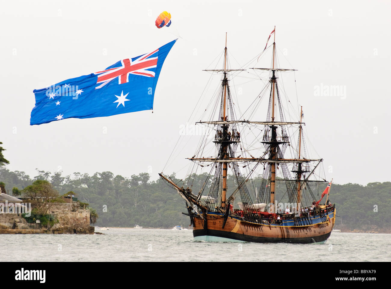 Replica del Capitano Cook nave a vela HM corteccia adopera nel porto di Sydney, con una grande bandiera australiana battenti nelle vicinanze. Foto Stock