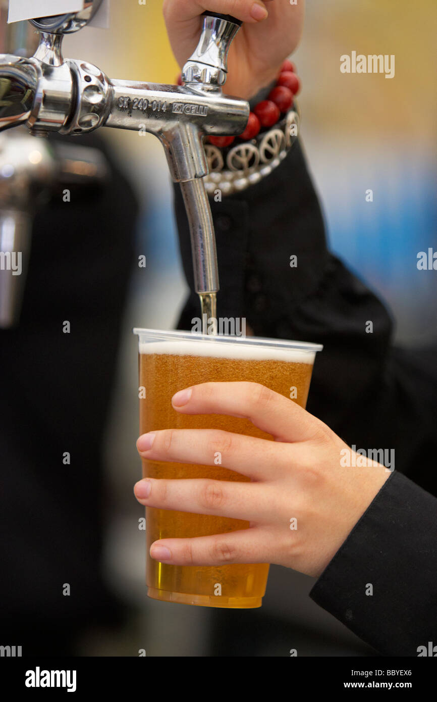 Barista femmina versando una pinta di birra in un bicchiere di plastica in una tenda di birra presso un festival Foto Stock
