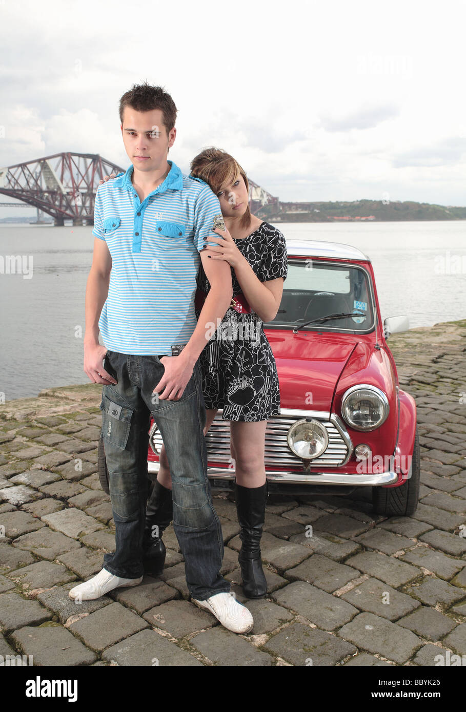 Ragazzo e ragazza modelli raffigurata con un rosso Mini Cooper su un molo dominato dal Ponte di Forth Rail nei pressi di Edimburgo. Foto Stock