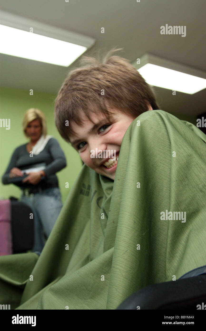 Sorridente ragazzo seduto nella sedia di stilisti prima di ottenere un taglio di capelli Foto Stock