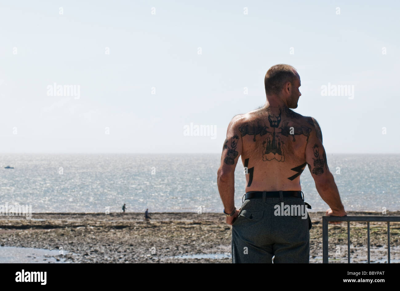 Un uomo coperto di tatuaggi e guardando sopra la spiaggia di Sully nel Galles del Sud. Foto Stock