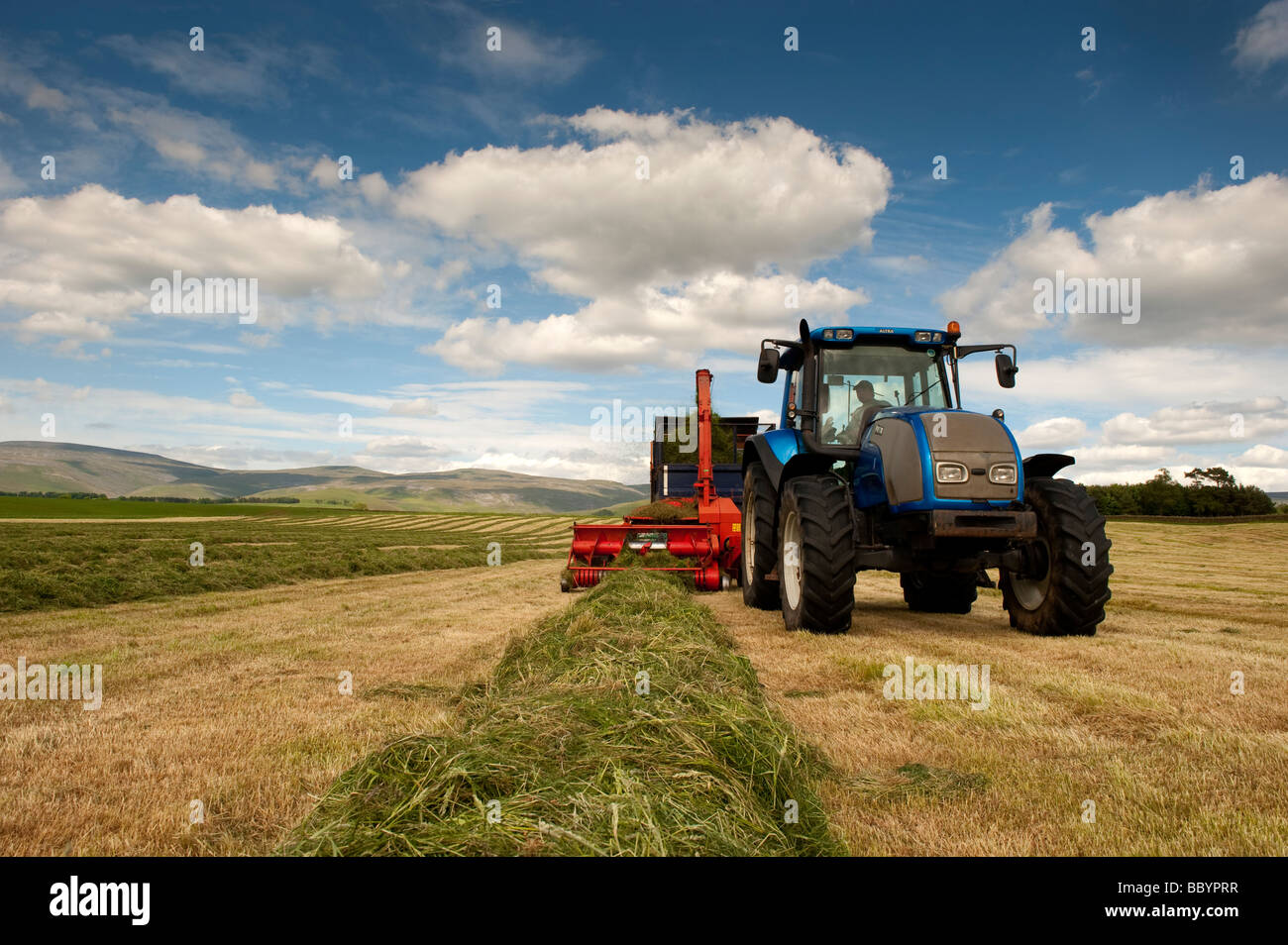 Trattore Valtra tirando un Kverneland trincia e rimorchio rendendo silaggio per bestiame Cumbria Inghilterra England Foto Stock