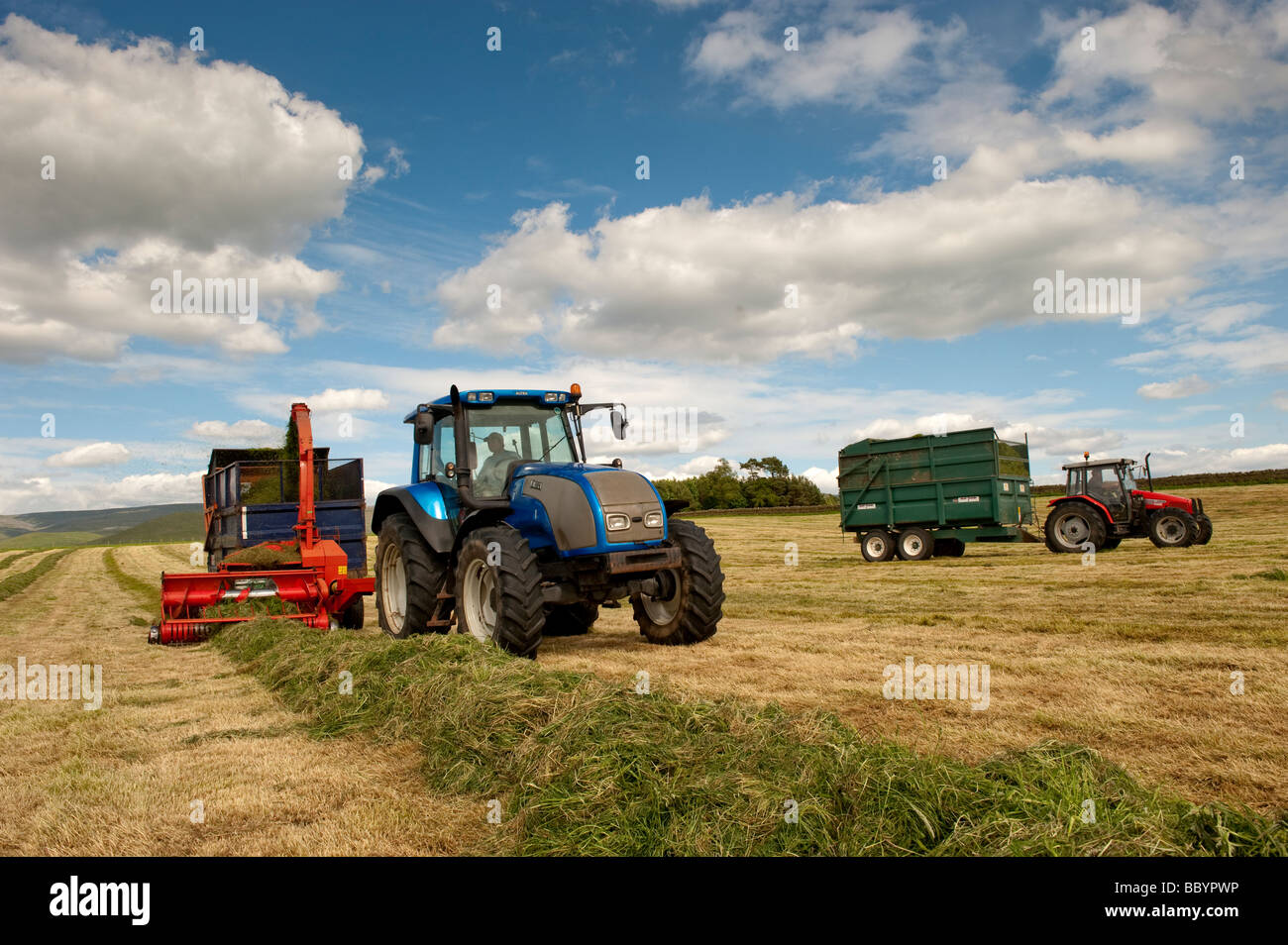 Trattore Valtra tirando un Kverneland trincia e rimorchio rendendo silaggio per bestiame Cumbria Inghilterra England Foto Stock