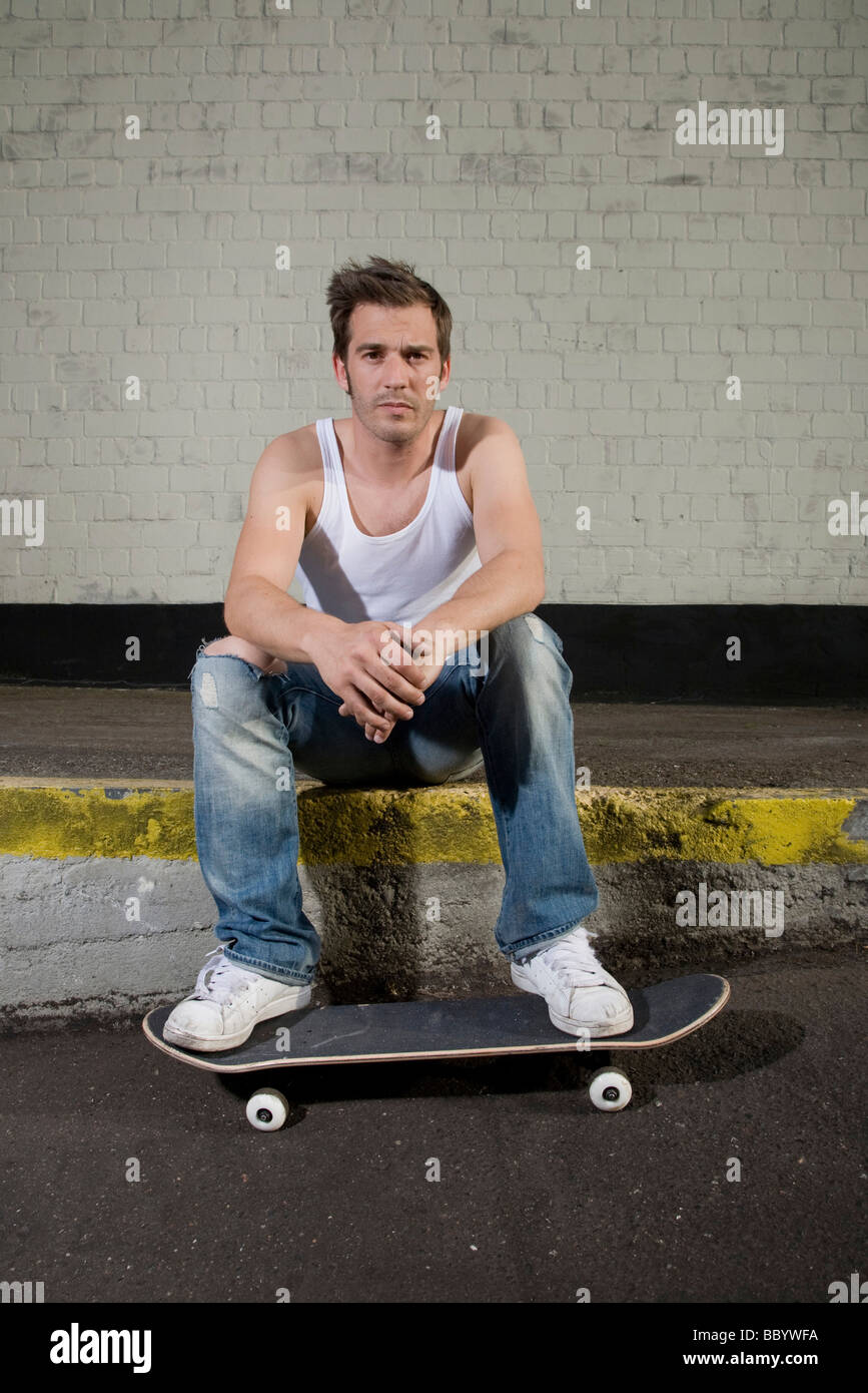 Guidatore di skateboard seduto su una rampa di carico, rilassato Foto Stock