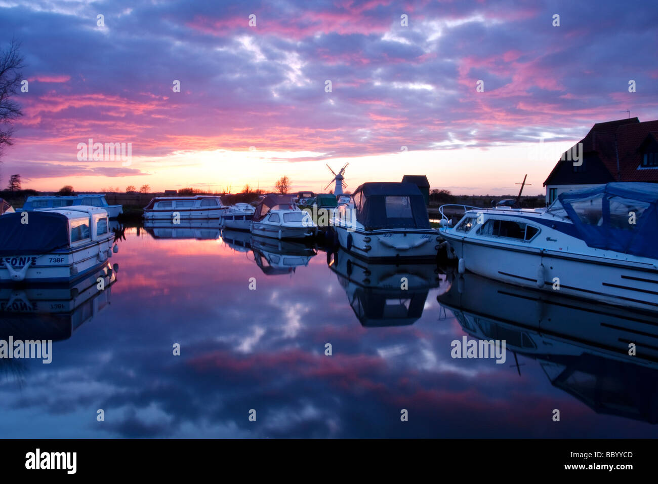 Staithe e barche a Thurne Dyke con il mulino a vento di Thurne in background al tramonto sulla Norfolk Broads Foto Stock